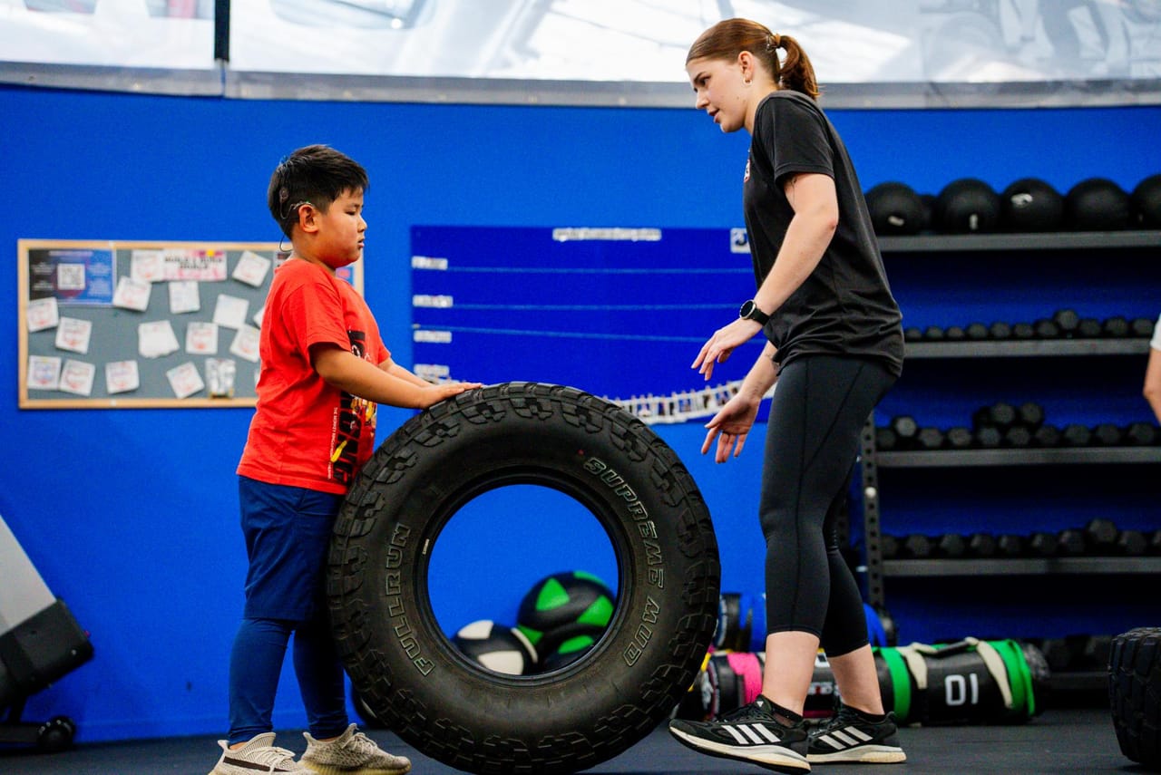 A young athlete flipping a tyre with a coach at the Junior Movement Academy
