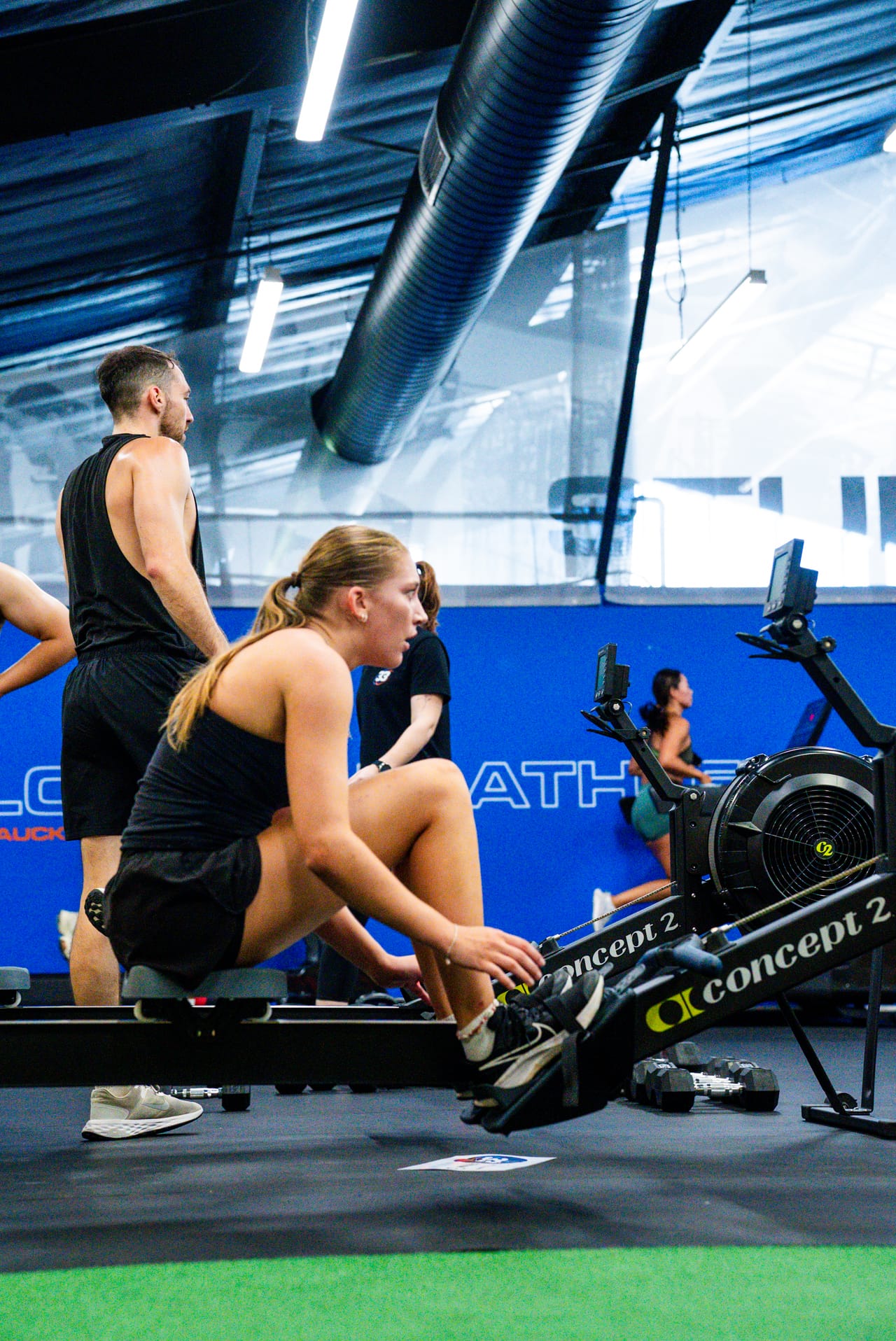 A member training on the rower with a coach during a conditioning class