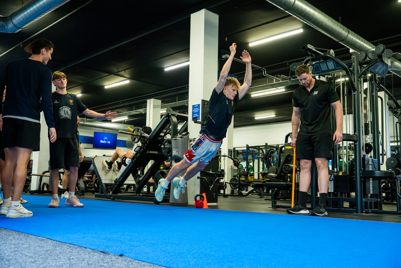 A young athlete performing a coached plyometric jump while coaches watch